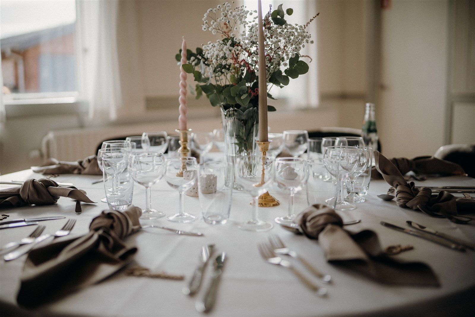 Mesa de boda con cristalería, vajilla blanca, velas y flores naturales. Fotografía de ambiente referencial.
